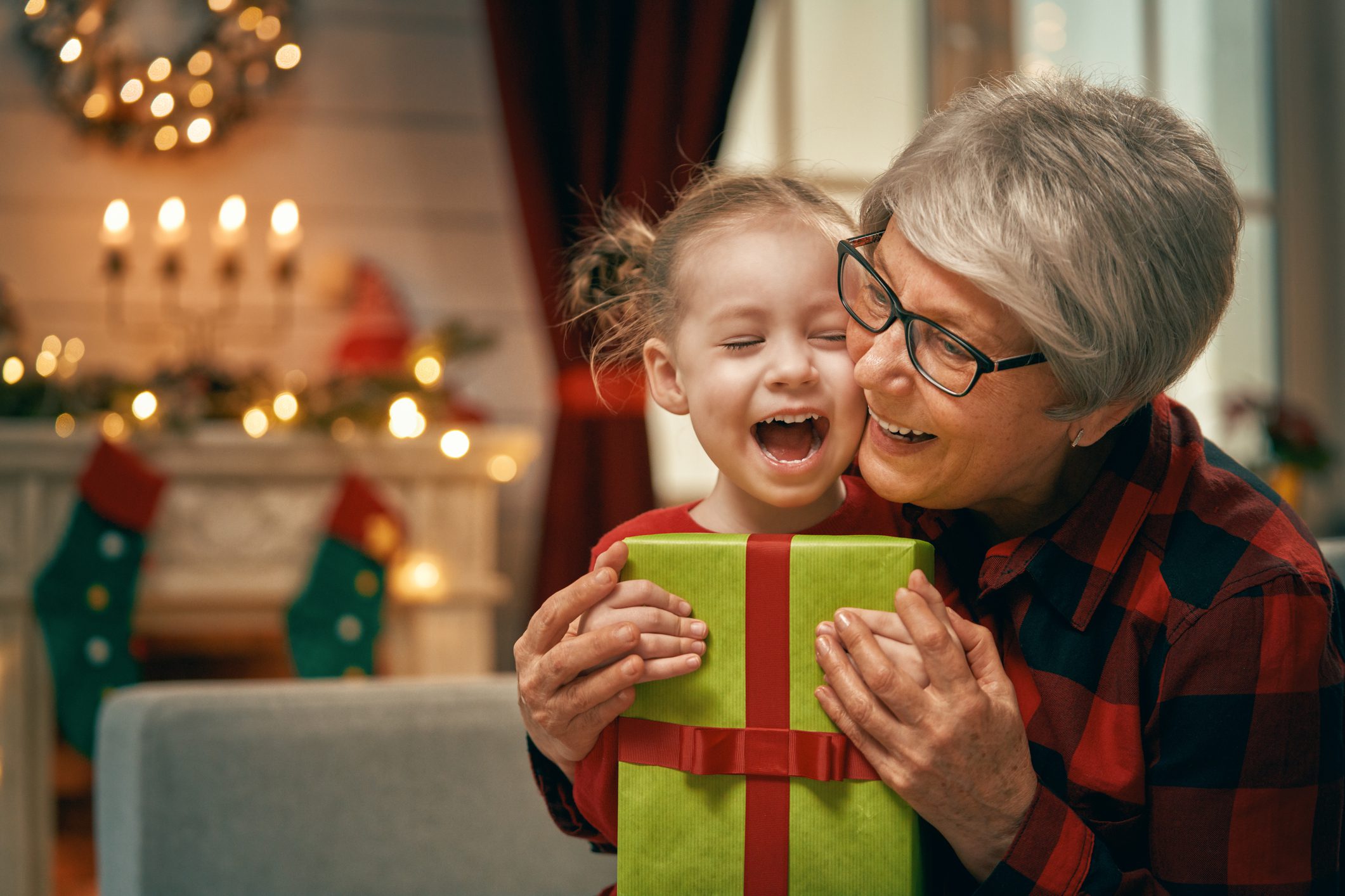 A grandmother hugs her granddaughter who is holding a holiday present.